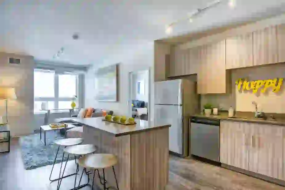 Kitchen island showing washed wood style cabinetry, dark counter-tops, and living area in the background