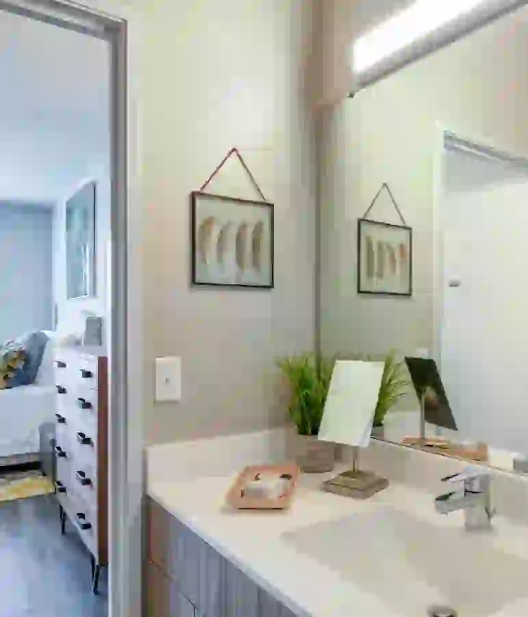 Student bathroom directly off bedroom showing white countertop, stainless sink faucet, and washed wood style cabinetry